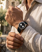 Person wearing a black wristwatch with a detailed face, outdoors.